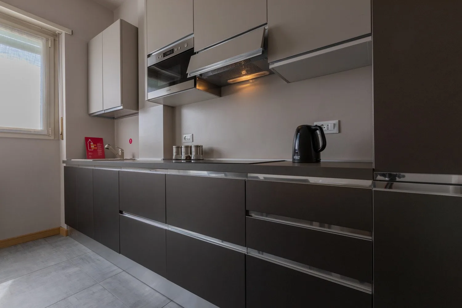 A modern kitchen with dark lower cabinets, a countertop, and a window.
