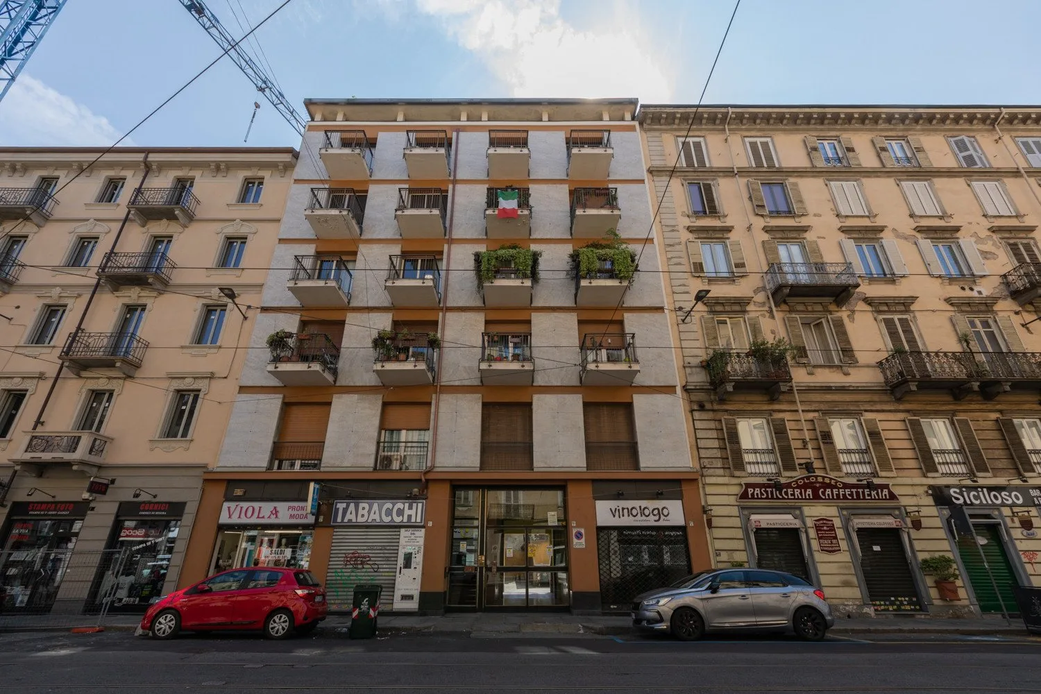 Street view of a multi-story building with balconies and ground-floor shops.