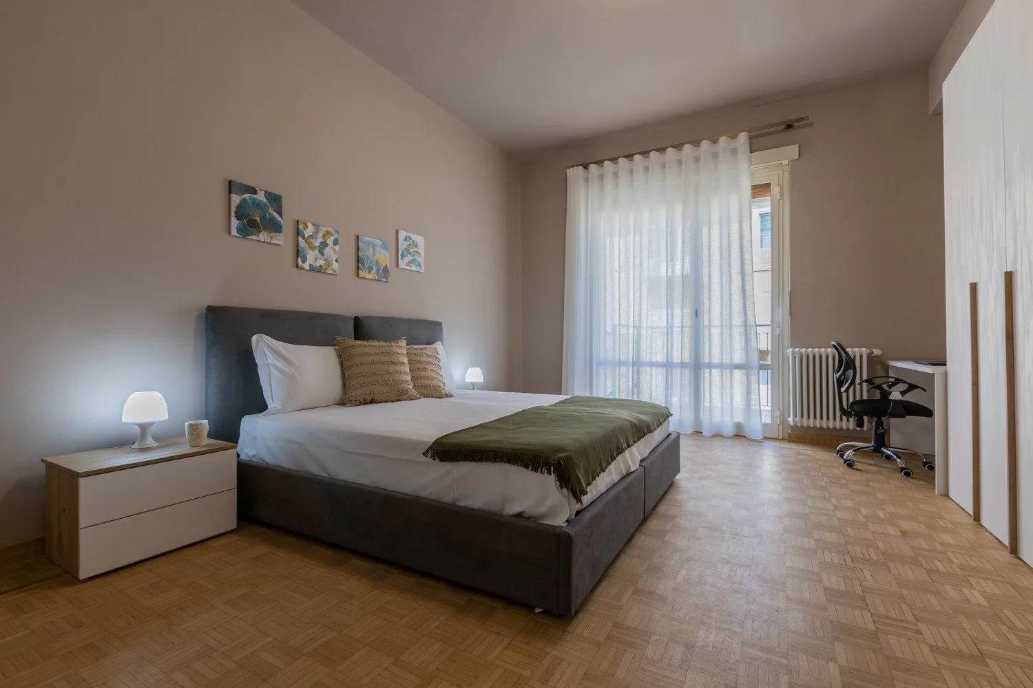 A bedroom with a bed, bedside table, and sheer curtains over the window.