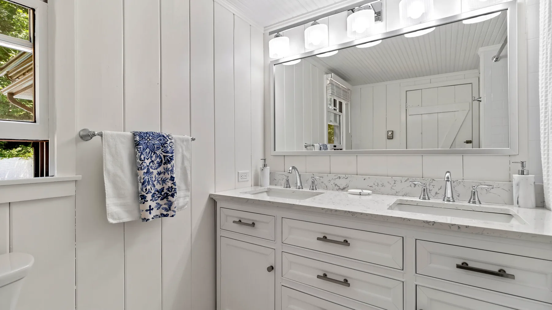 Un baño luminoso con un mueble de lavabo largo, espejo y toalla de manos estampada.