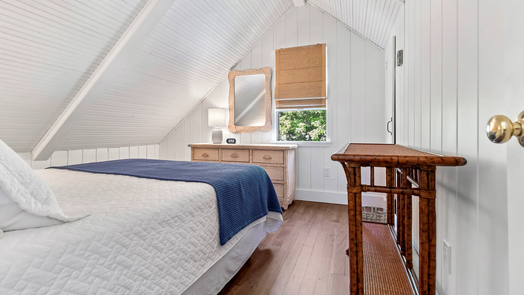 Un dormitorio abuhardillado luminoso con una cama bajo un techo blanco inclinado.
