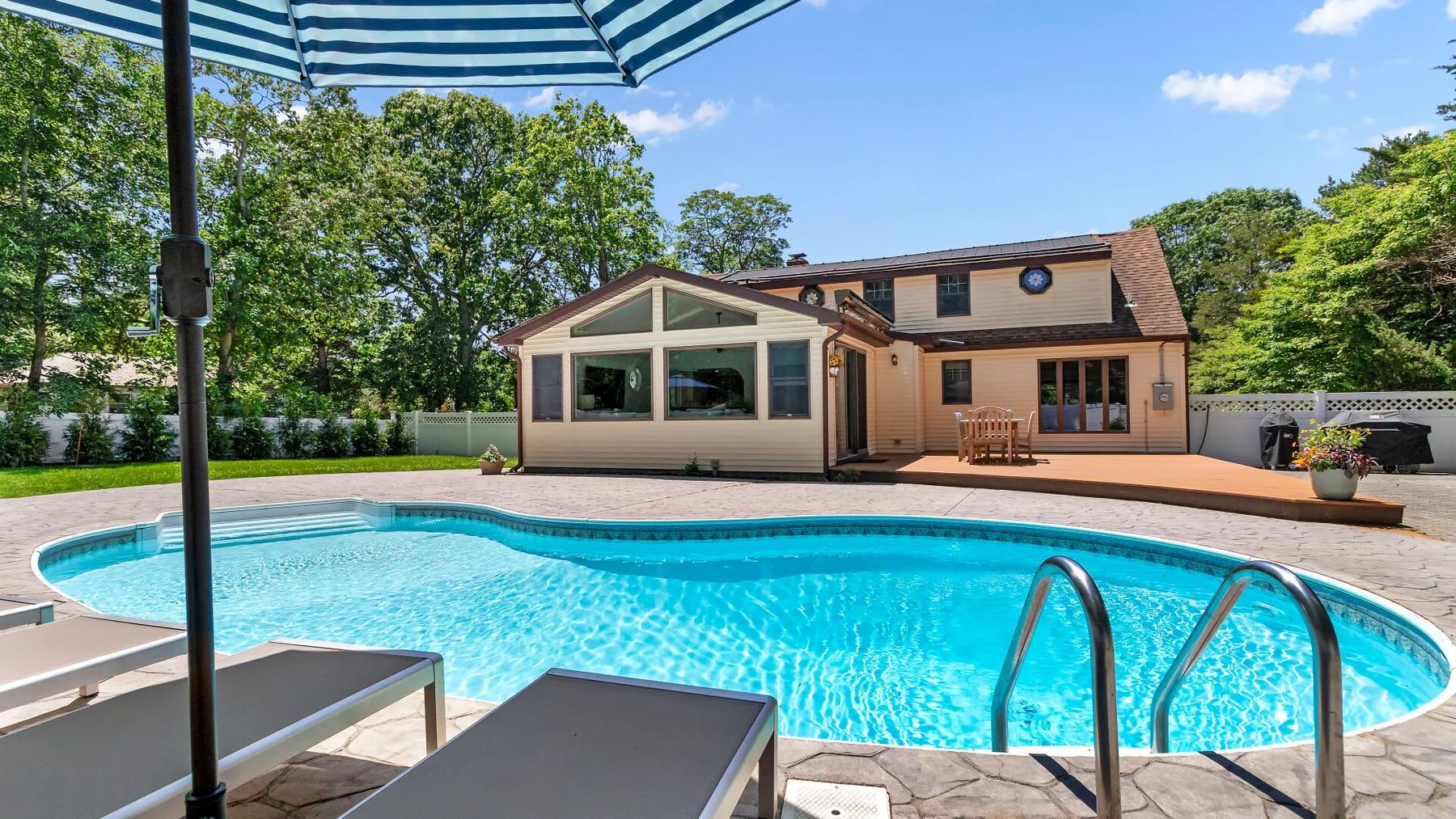 Una piscina al aire libre está junto a una casa, con asientos para descansar cerca.