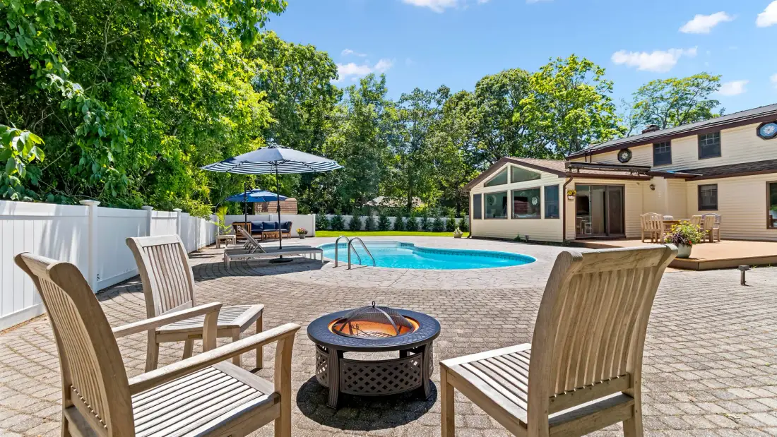 An outdoor pool patio with seating and a fire pit beside a house.