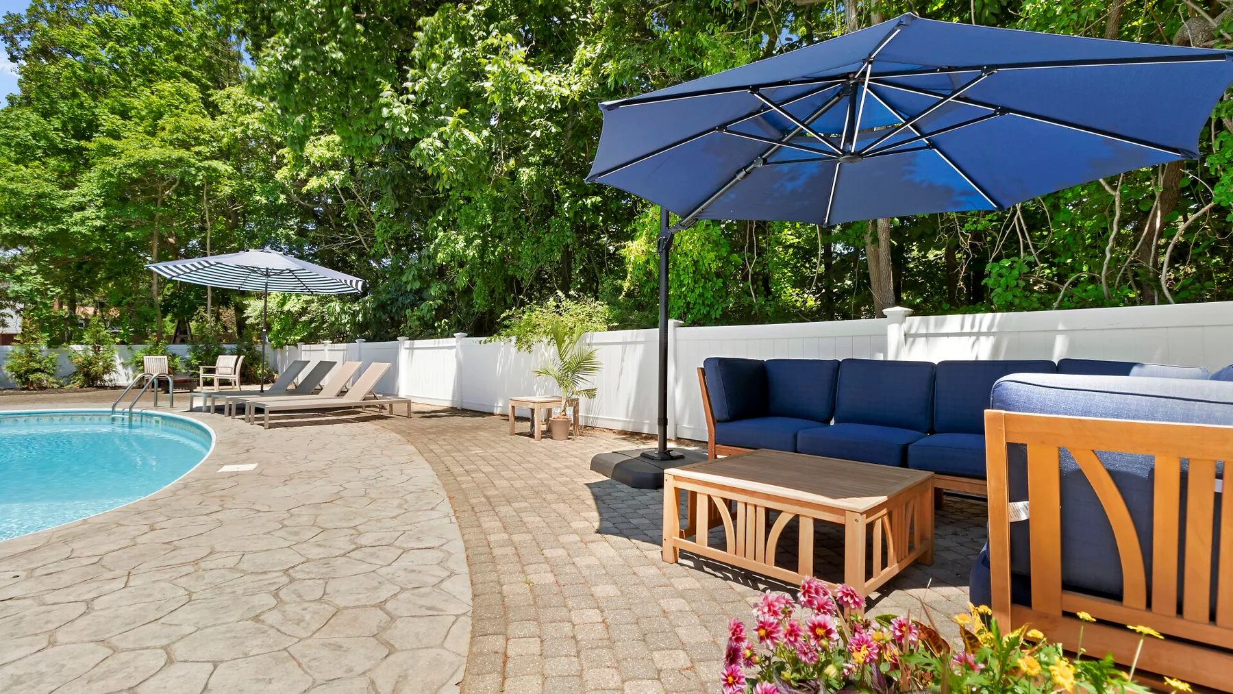 Un patio con piscina al aire libre y asientos acolchados bajo una sombrilla azul.