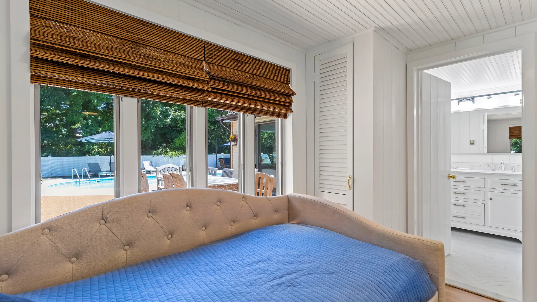 Un dormitorio con una cama cubierta de azul junto a ventanas que dan a una piscina.