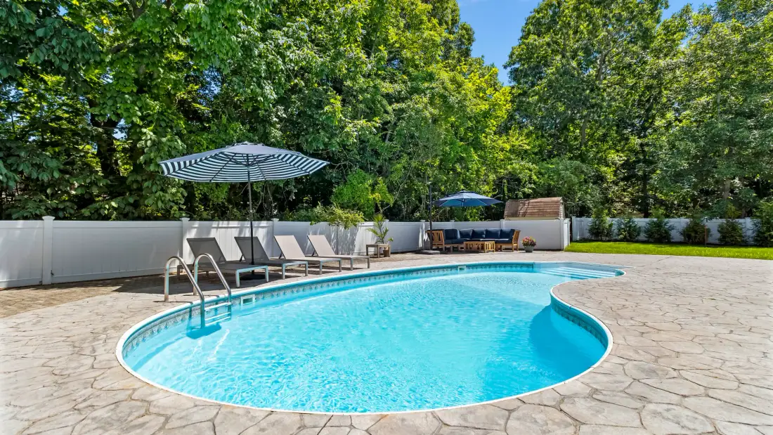 Una piscina al aire libre con asientos y sombrillas junto a una terraza pavimentada.
