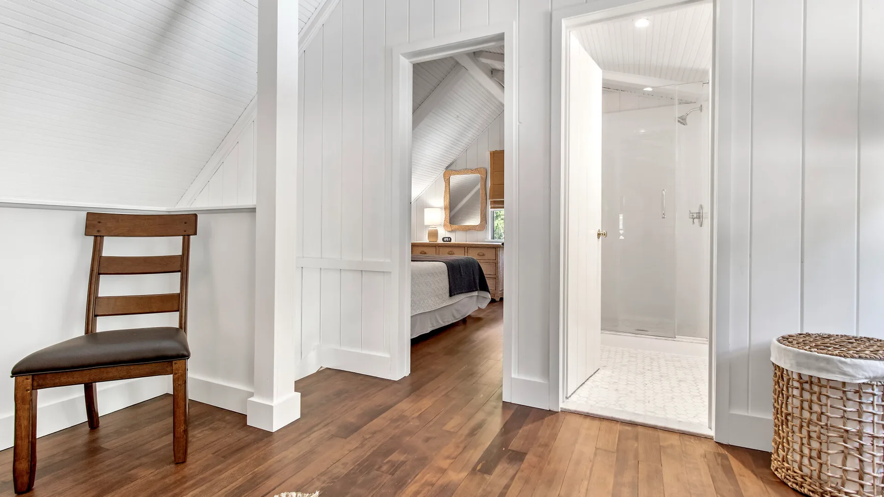 Un dormitorio luminoso con una silla de madera, una cama y un baño contiguo.