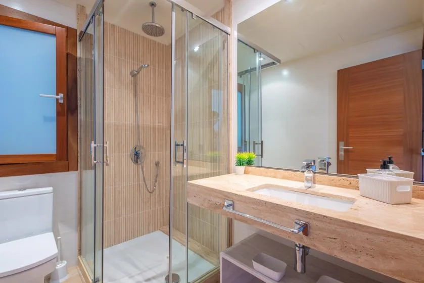 A bathroom with a glass shower and a long countertop sink.