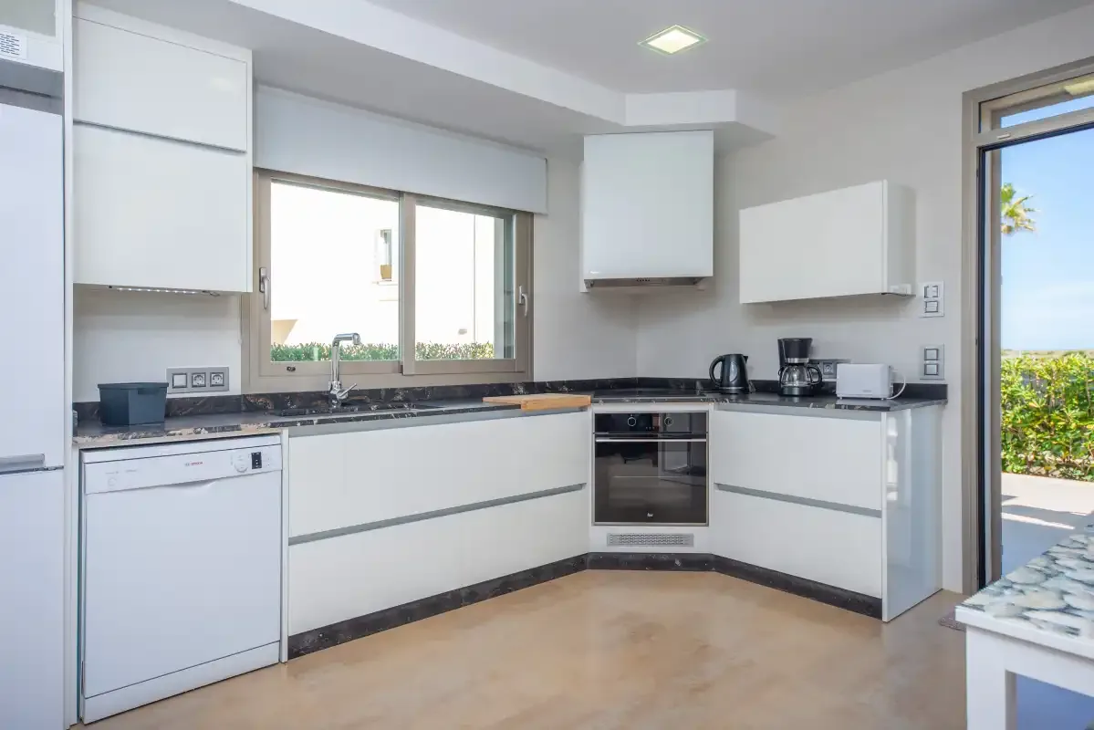 A bright modern kitchen with white cabinets and dark countertops.