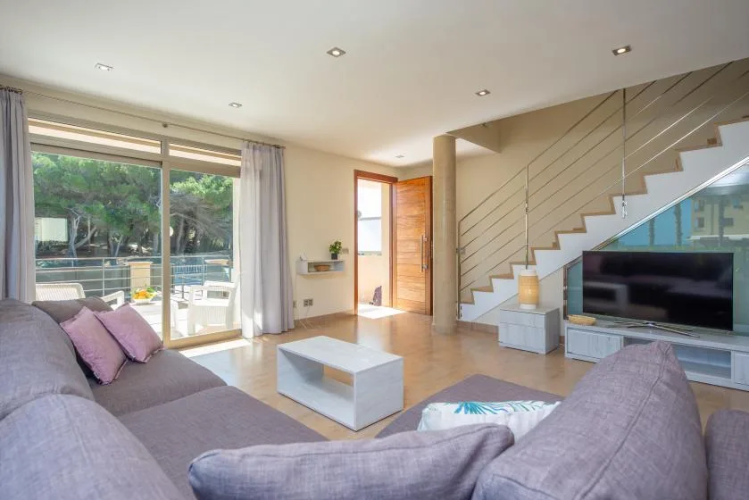 A bright living room with seating, a television, and glass doors opening to a patio.