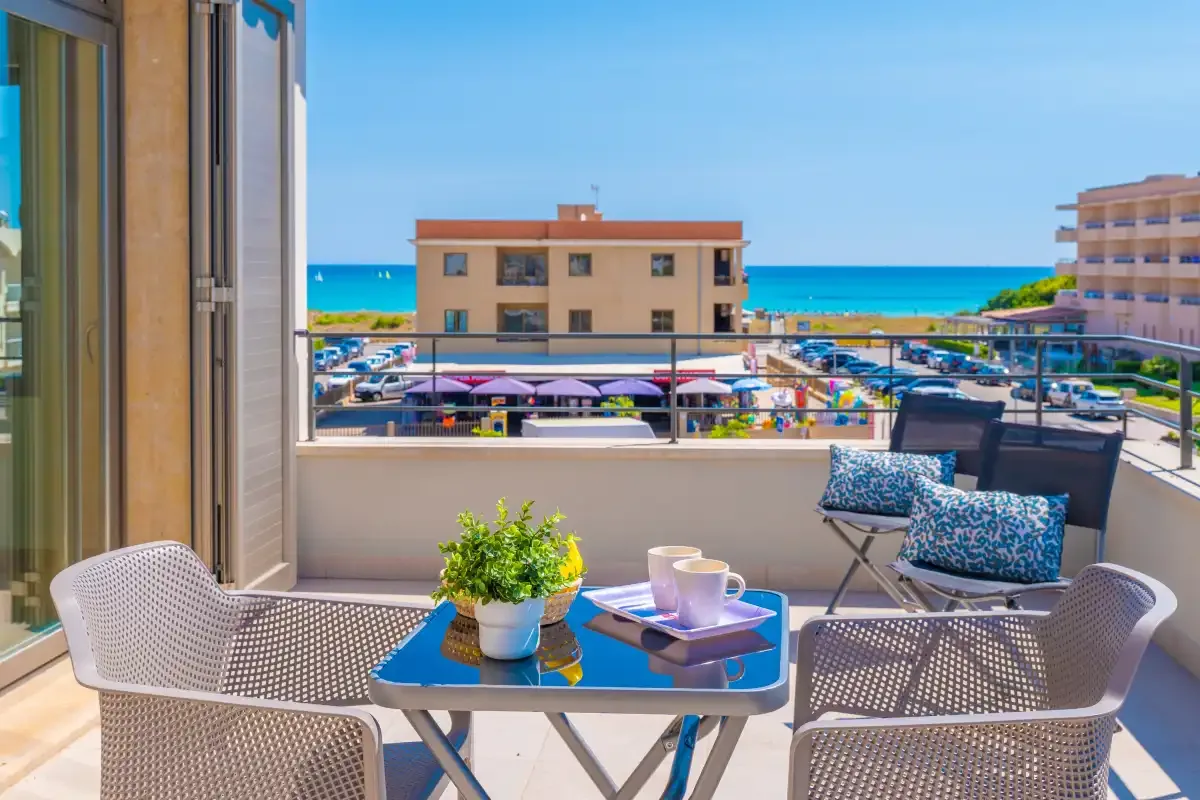 A furnished balcony overlooks nearby buildings and the sea.