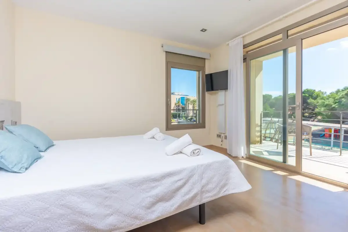 A bright bedroom with a bed beside glass doors opening onto a balcony.