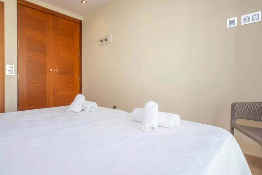A bedroom with a white bed and folded towels beside wooden doors.
