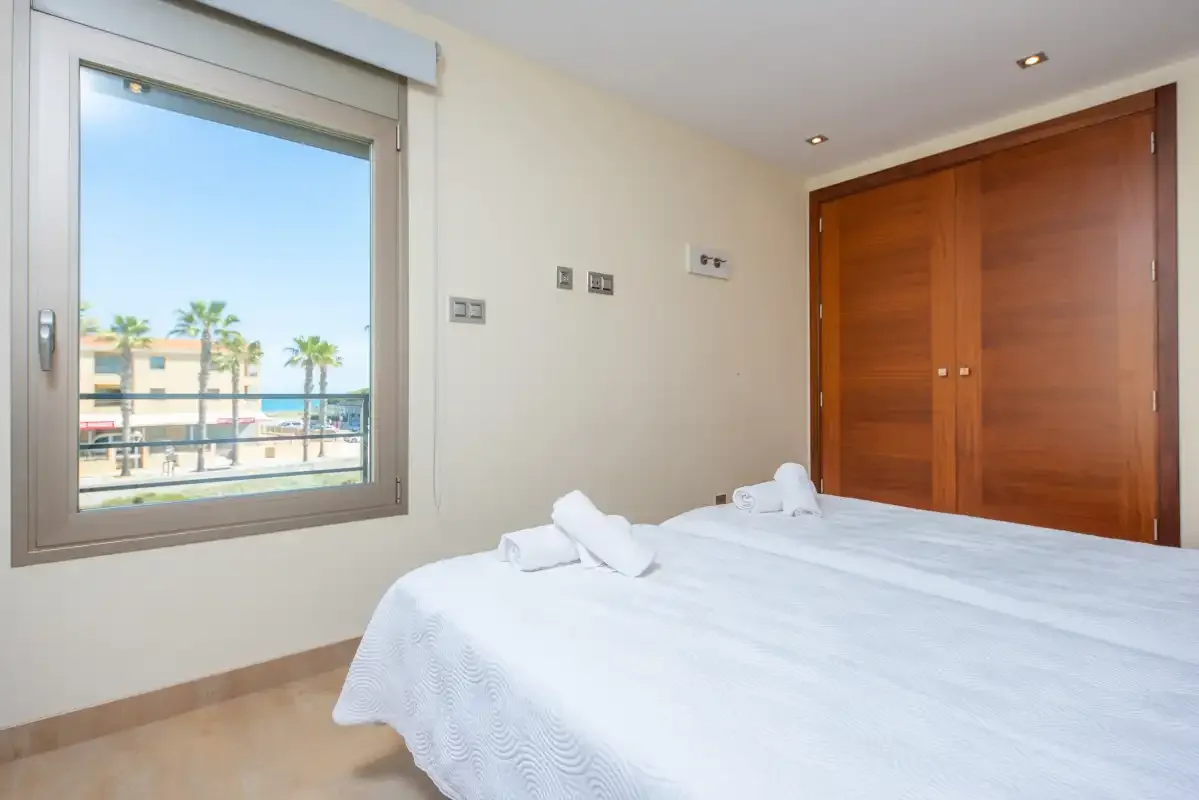 A bedroom with white bedding and a window overlooking palm trees.