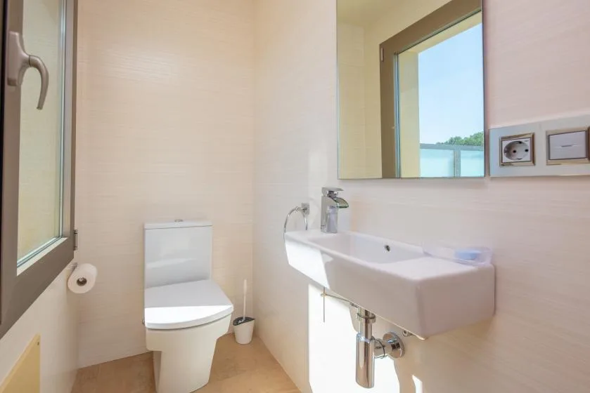 A bright bathroom with a toilet, sink, and window overlooking the water.