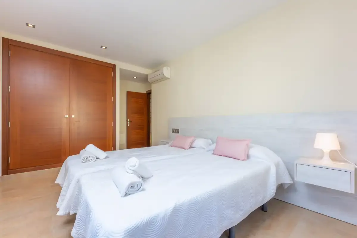 A bedroom with a neatly made bed, pink pillows, and a wooden wardrobe.