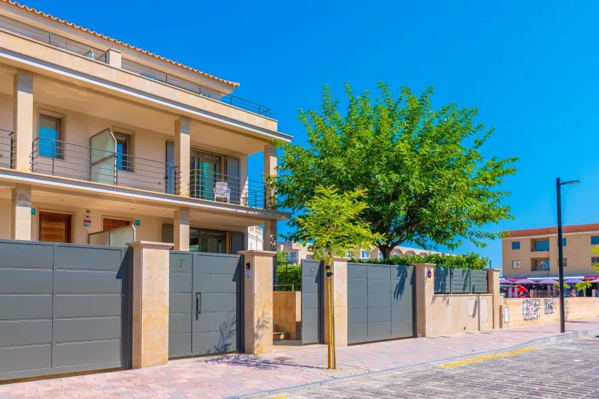 A modern multi-story building stands behind a gated street frontage, with a leafy tree nearby.