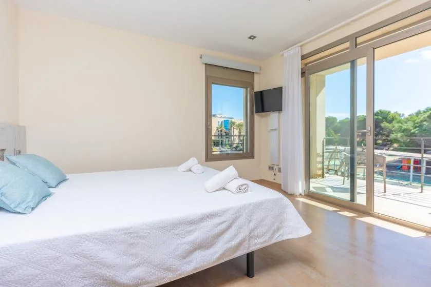 A bright bedroom with a bed beside large glass doors opening onto a balcony.
