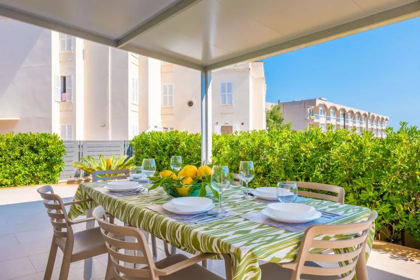 Comedor exterior cubierto con una mesa preparada junto a setos verdes.