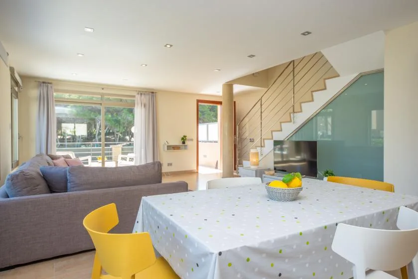 A bright living and dining area with a table, seating, and a staircase.