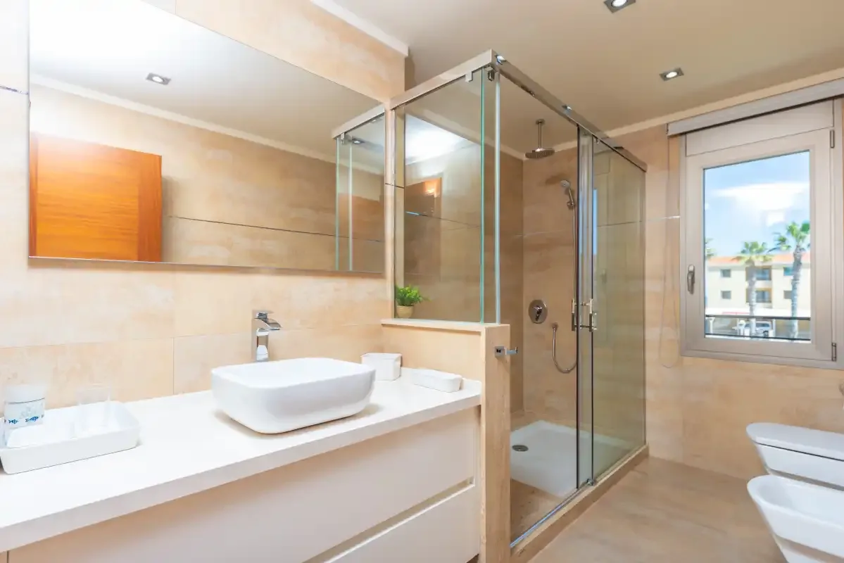 A tiled bathroom with a glass shower, sink, and window.