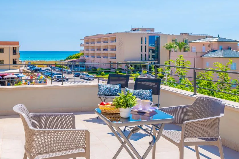 Una terraza en la azotea con mesa y asientos tiene vistas a edificios cercanos y al mar.