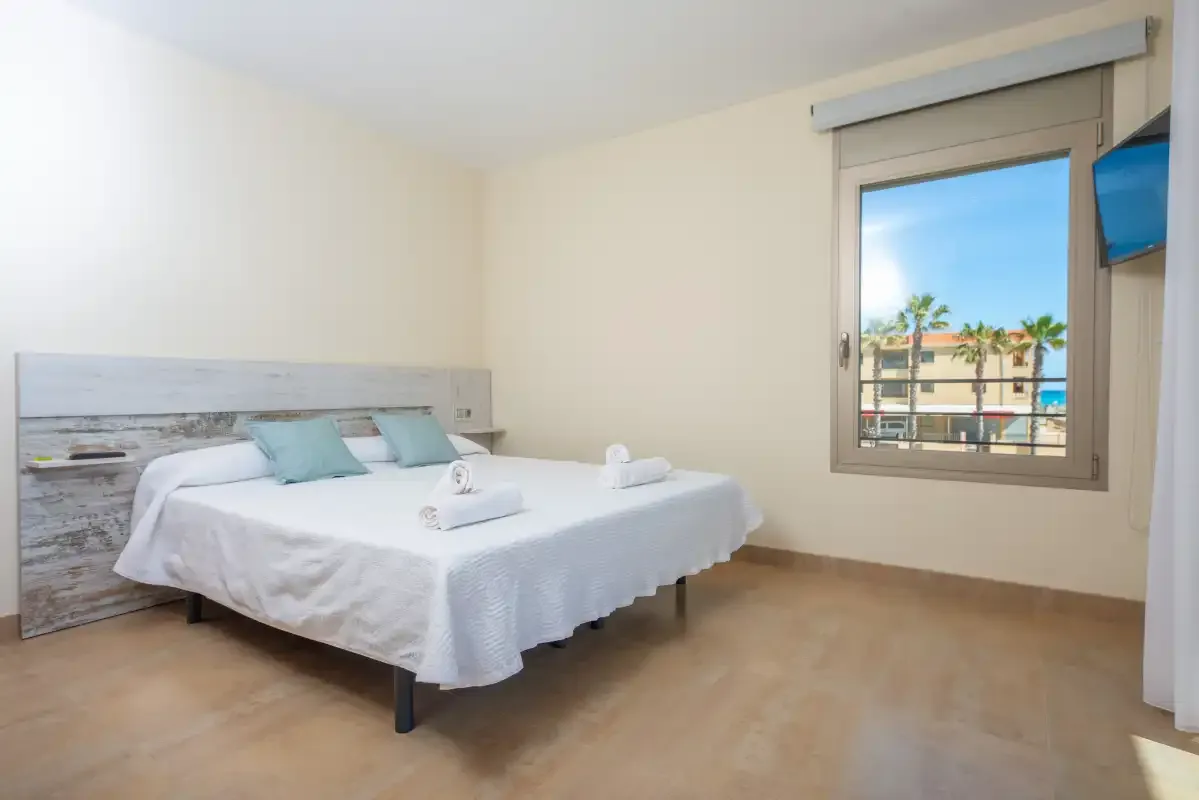 A bedroom with a neatly made bed and a window overlooking nearby buildings.