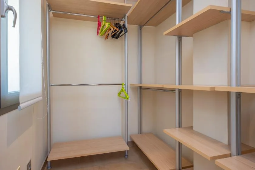 A walk-in closet with wooden shelves, hanging rails, and clothes hangers.
