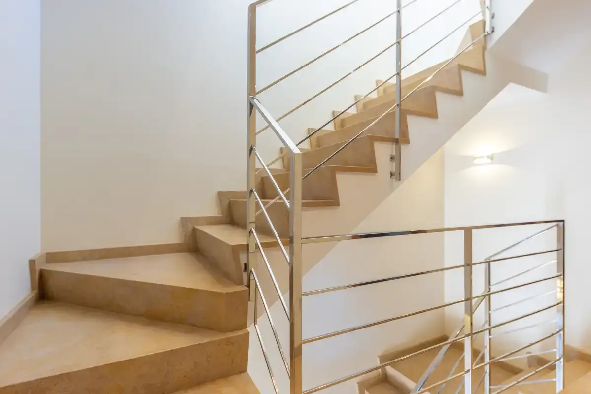 A staircase with wooden steps and metal railings rises beside a white wall.