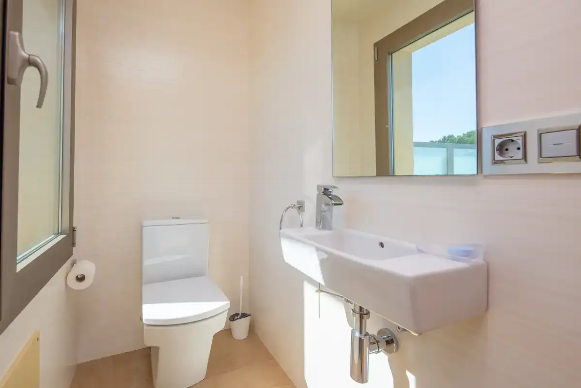 A bright bathroom with a toilet, sink, and window.