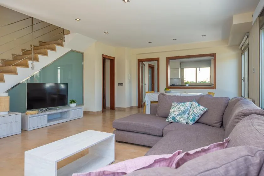 A living room with a sectional sofa, television, and staircase.