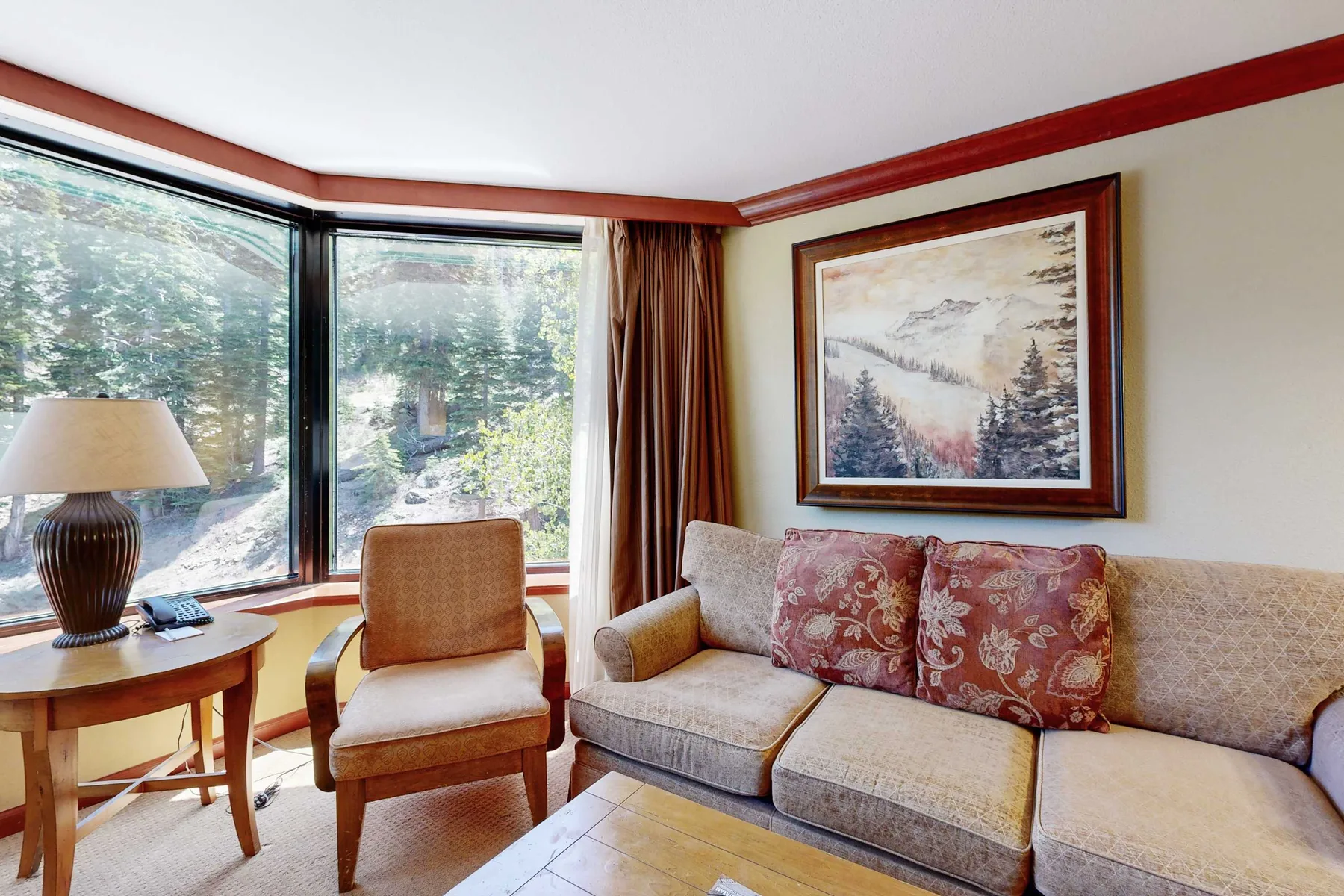 Una sala de estar con asientos junto a grandes ventanas y un cuadro de paisaje enmarcado.