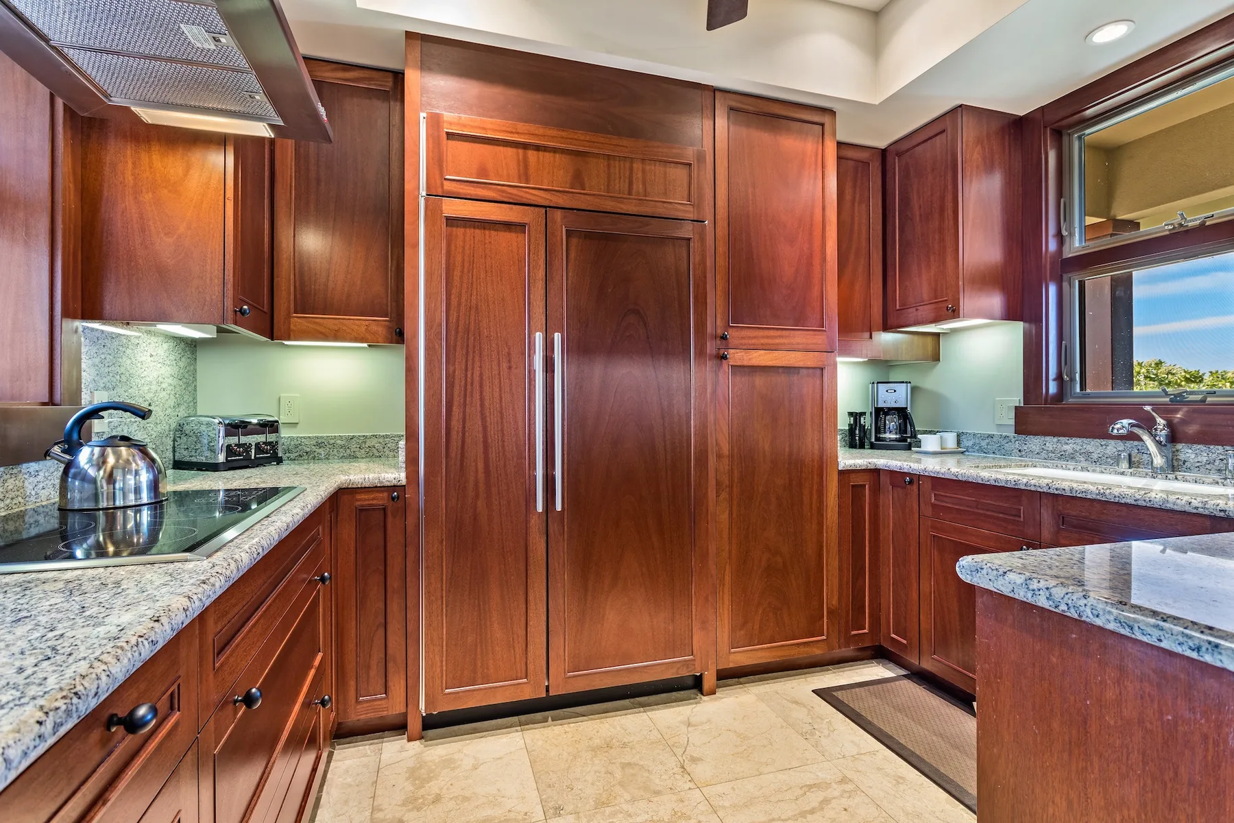 Una cocina con gabinetes de madera, encimeras de piedra y una tetera de acero inoxidable.