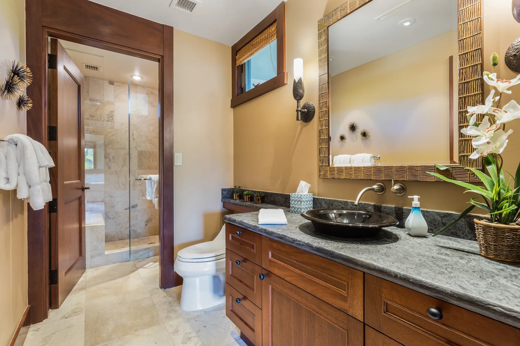 Un baño con un tocador oscuro, un lavabo sobre la encimera y un espejo grande enmarcado.
