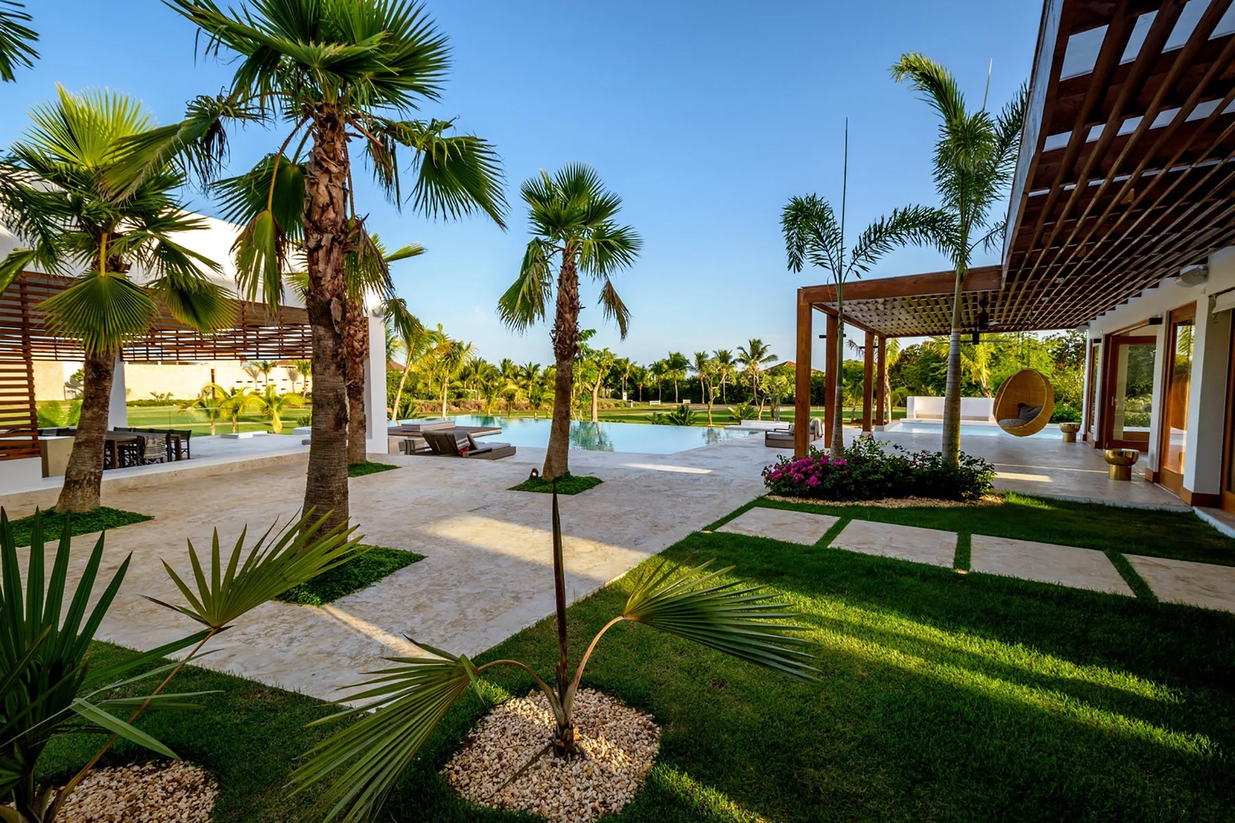 Un patio junto a la piscina con palmeras y zonas de estar cubiertas.