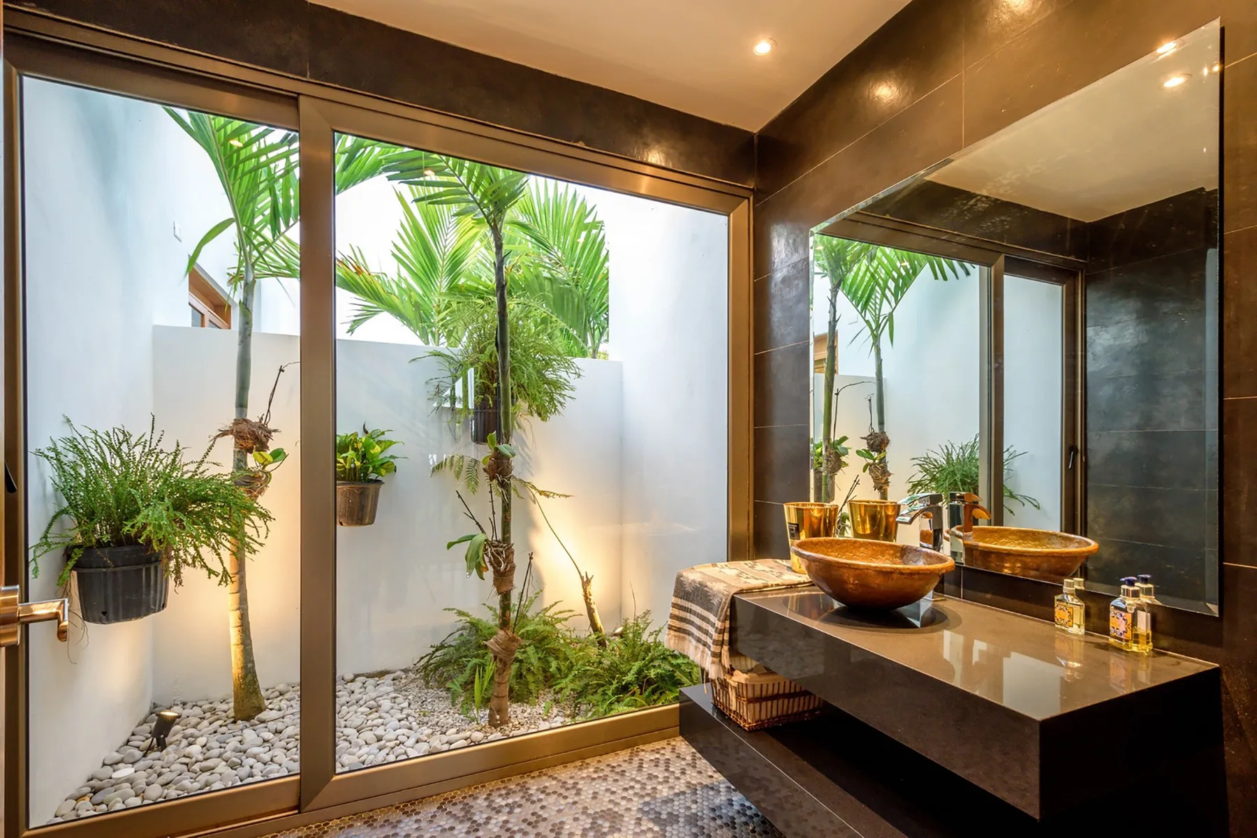 Un lavabo de baño está junto a puertas de vidrio que dan a un pequeño patio con plantas.