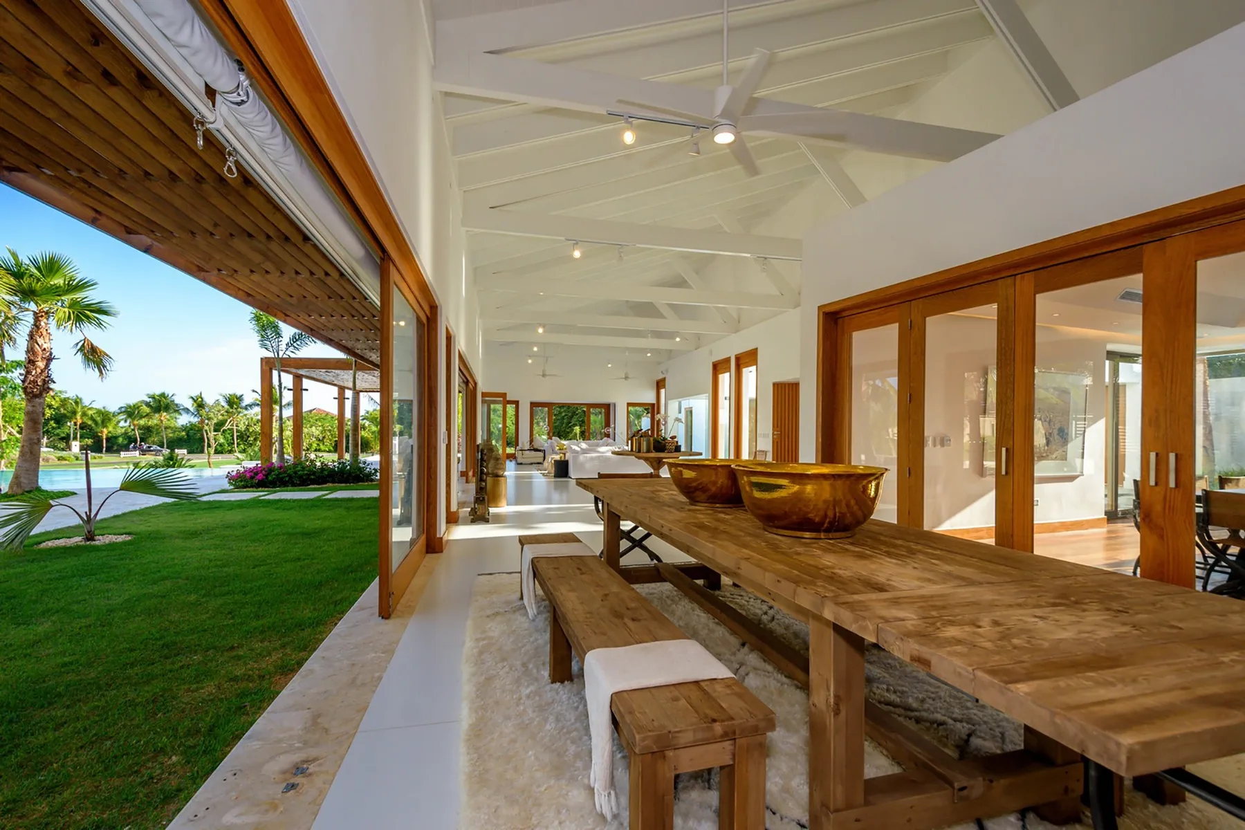 Un comedor abierto con una larga mesa de madera junto a grandes ventanales con vistas al jardín.