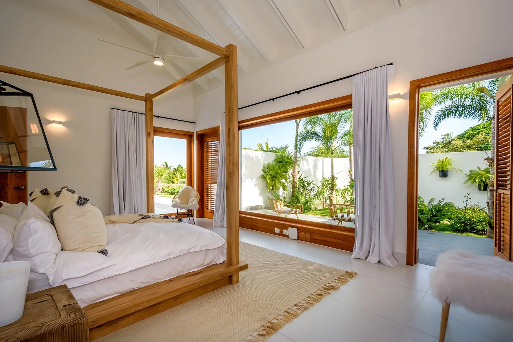 Un dormitorio luminoso con una cama de madera, grandes ventanales y vistas al jardín.