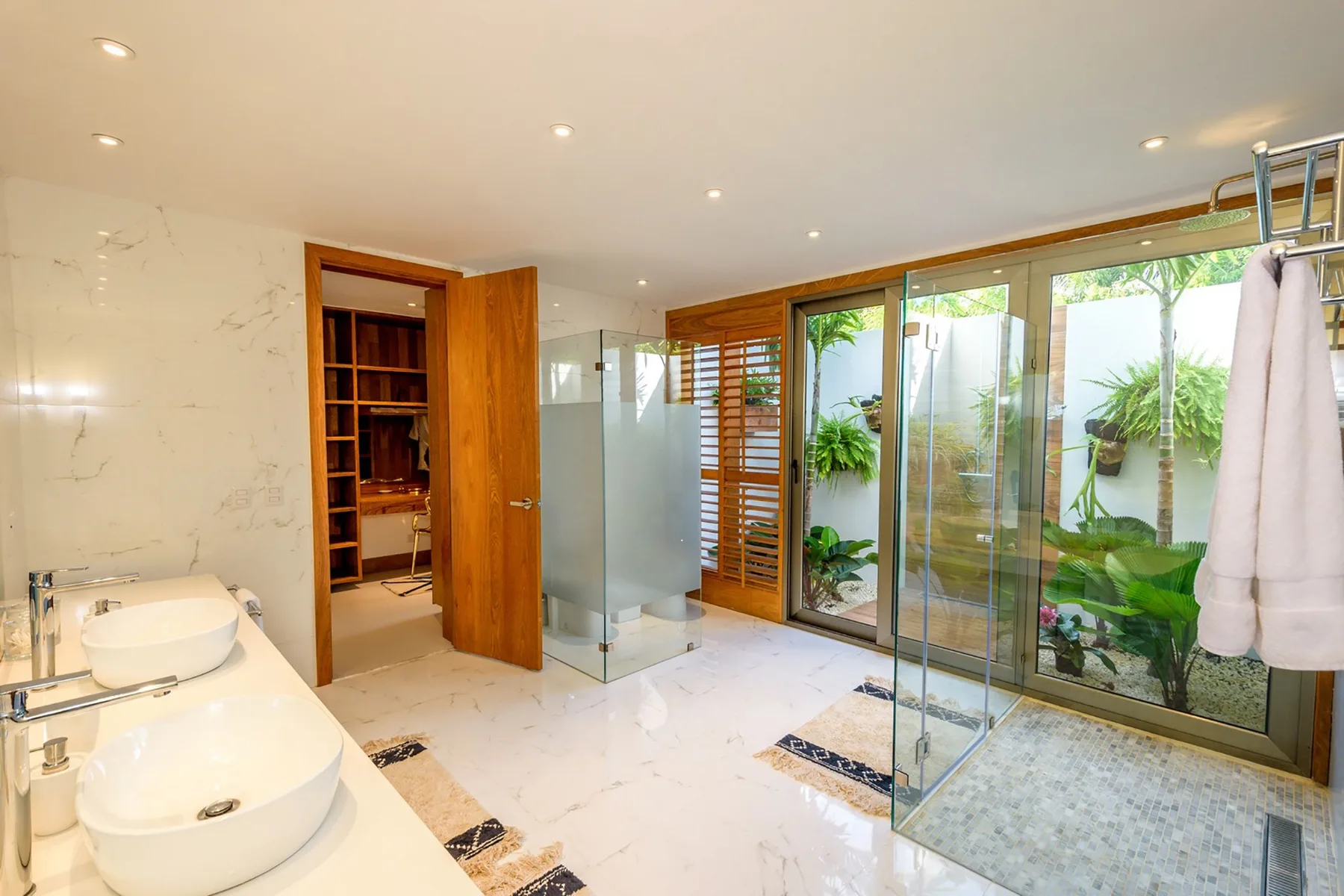 Un baño luminoso con ducha de vidrio y vistas a un patio con plantas.