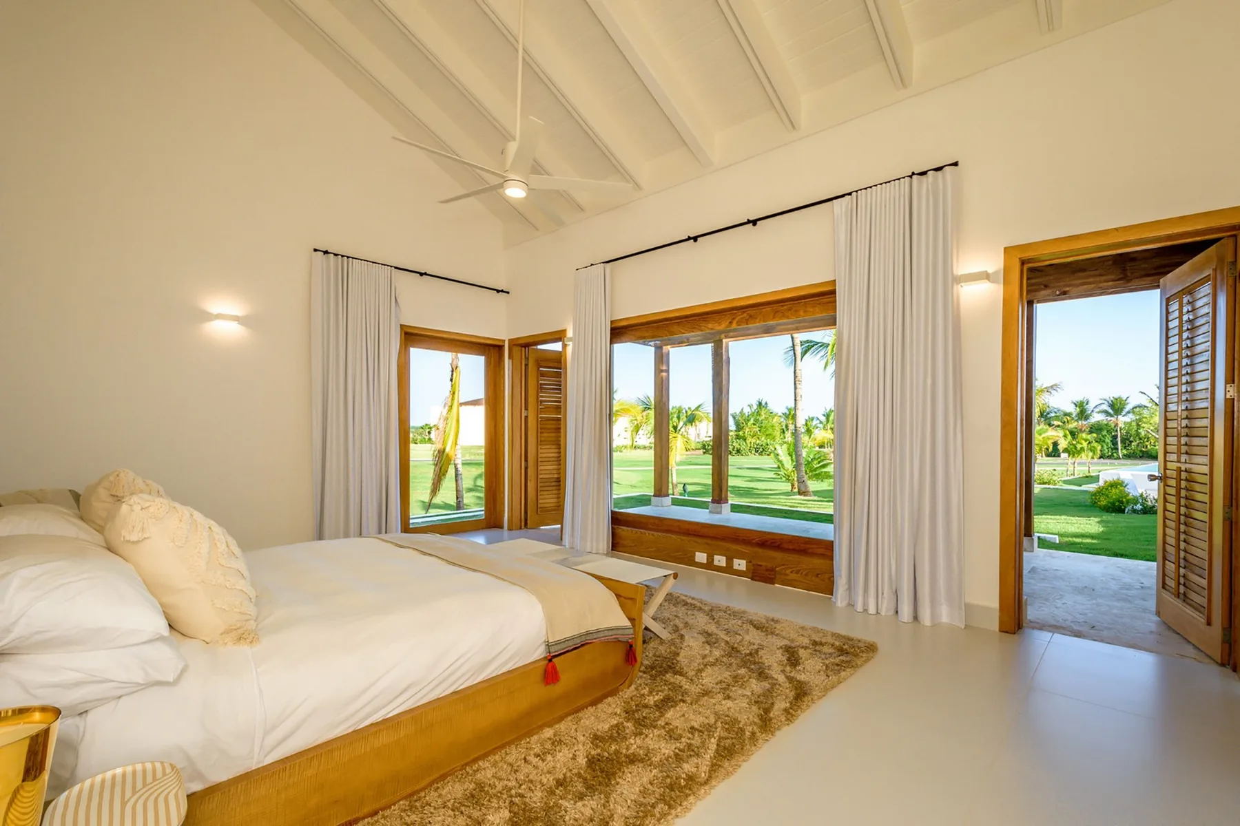 Un dormitorio luminoso con una cama, grandes ventanas y vistas a zonas verdes.