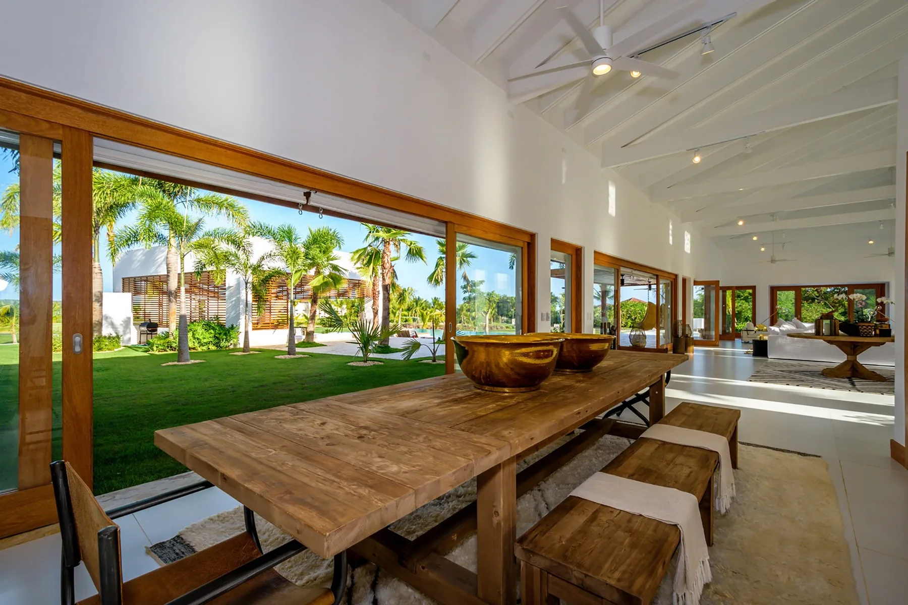 Un comedor luminoso con una larga mesa de madera junto a grandes ventanales que dan a un jardín.