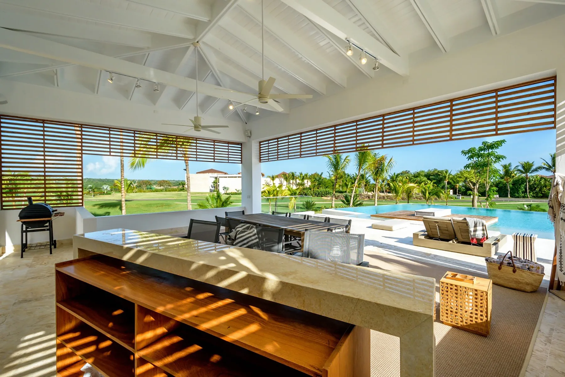 Una cocina y comedor al aire libre dan a una piscina y jardines.