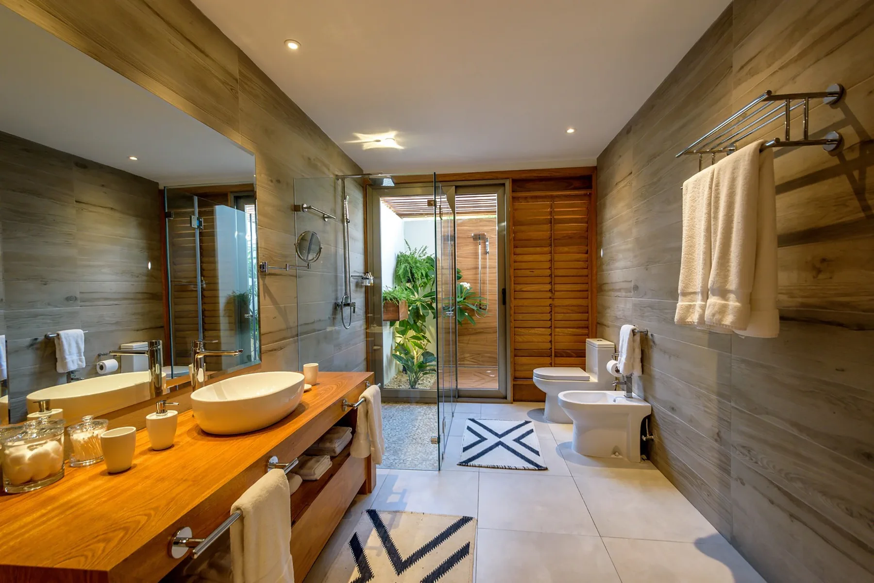 Un baño amplio cuenta con un tocador de madera, ducha de vidrio y accesorios blancos.