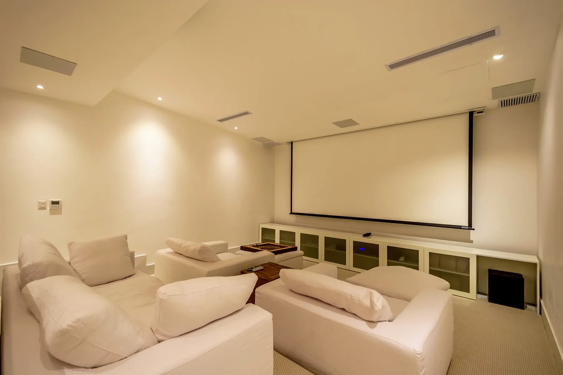 Una sala de cine en casa con una gran pantalla de proyección y asientos claros.