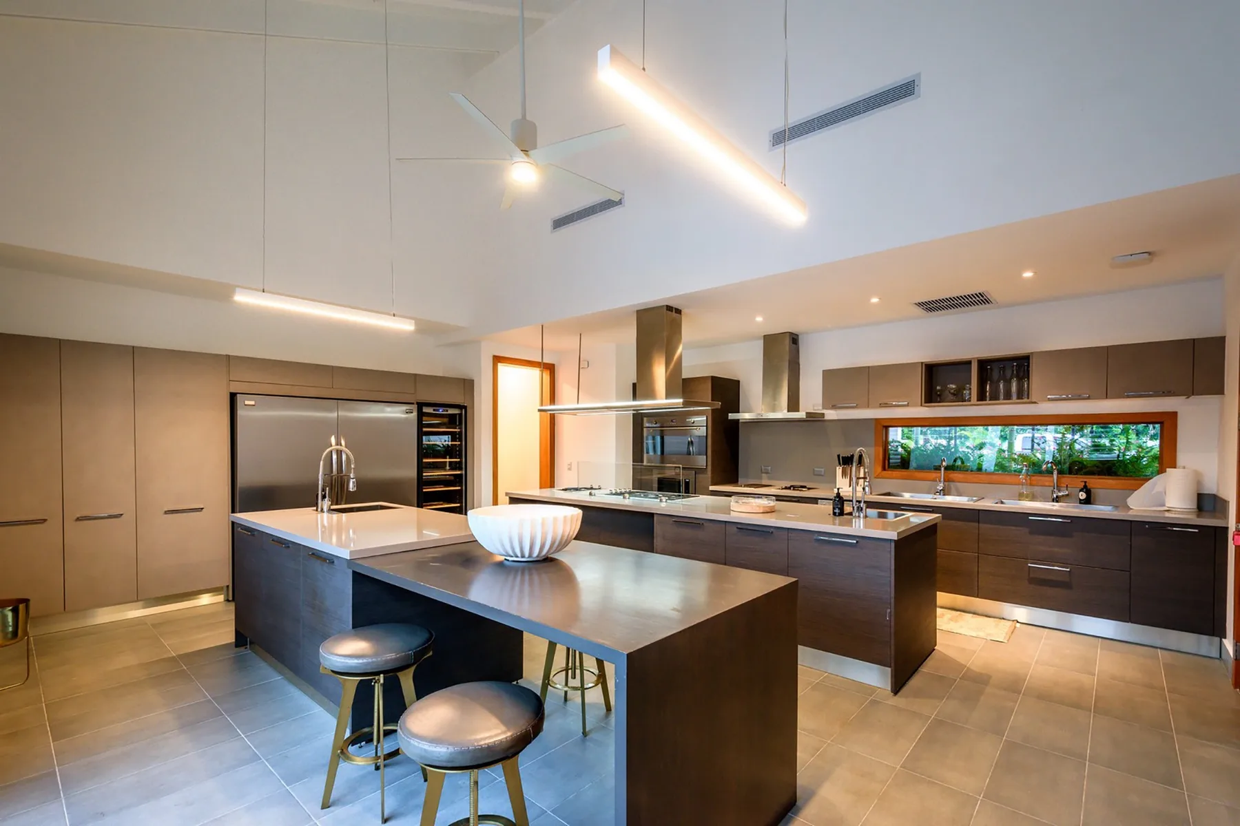 Una cocina moderna y amplia con gabinetes oscuros, amplias encimeras y una ventana alargada.