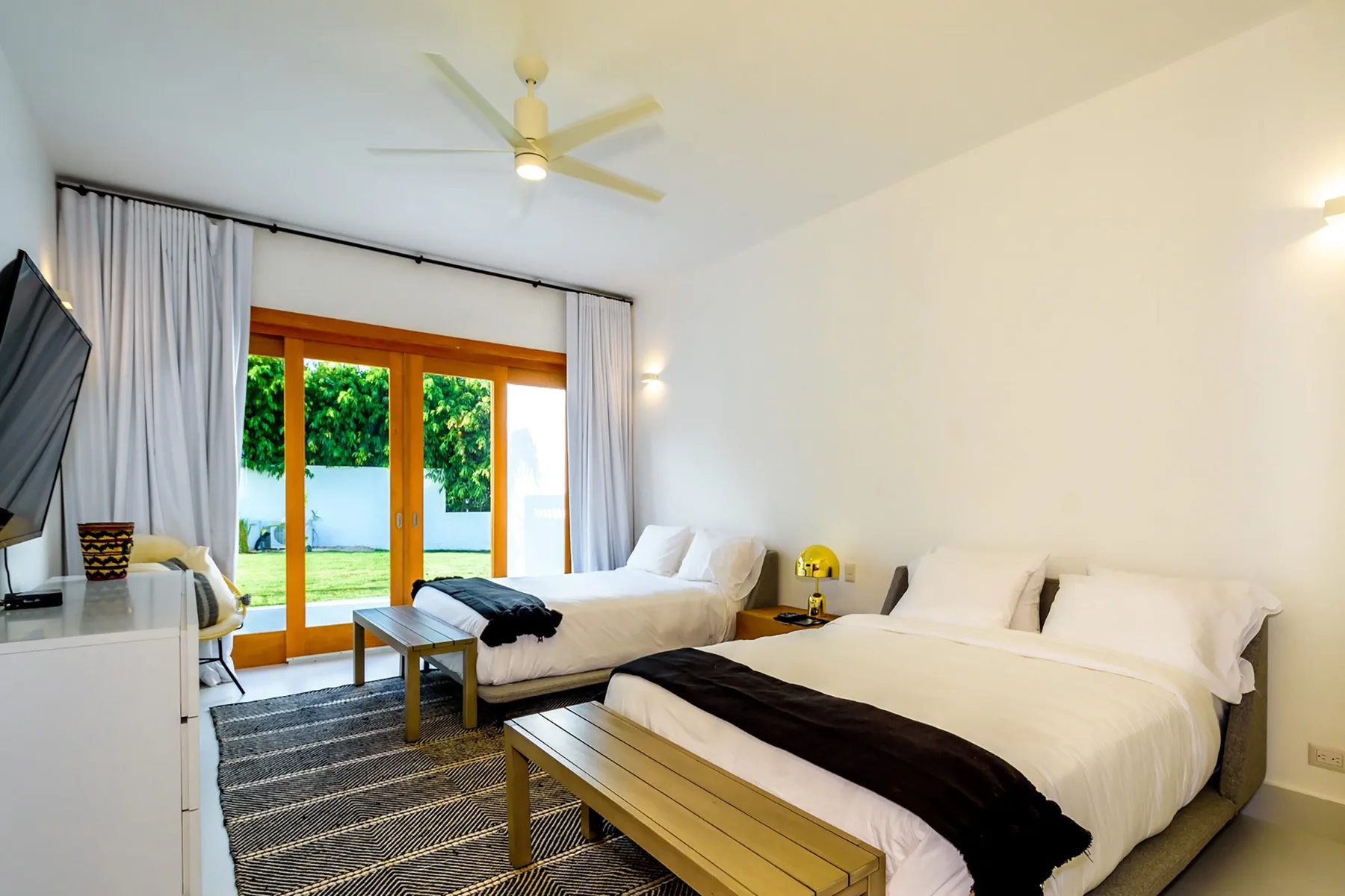 Un dormitorio luminoso con dos camas junto a grandes puertas de vidrio que dan a un jardín.