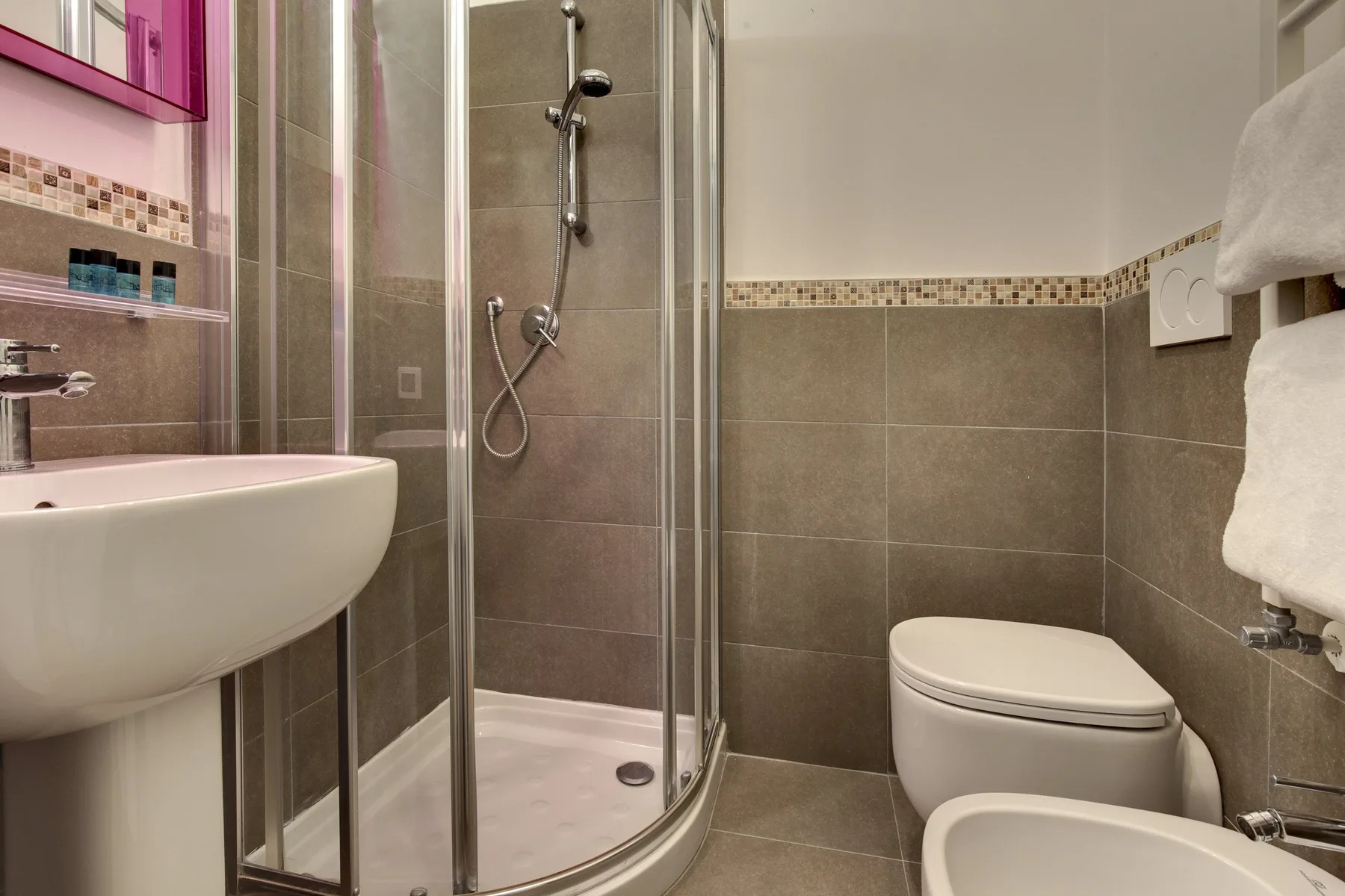 Un baño con azulejos, ducha de vidrio, lavabo e inodoro.