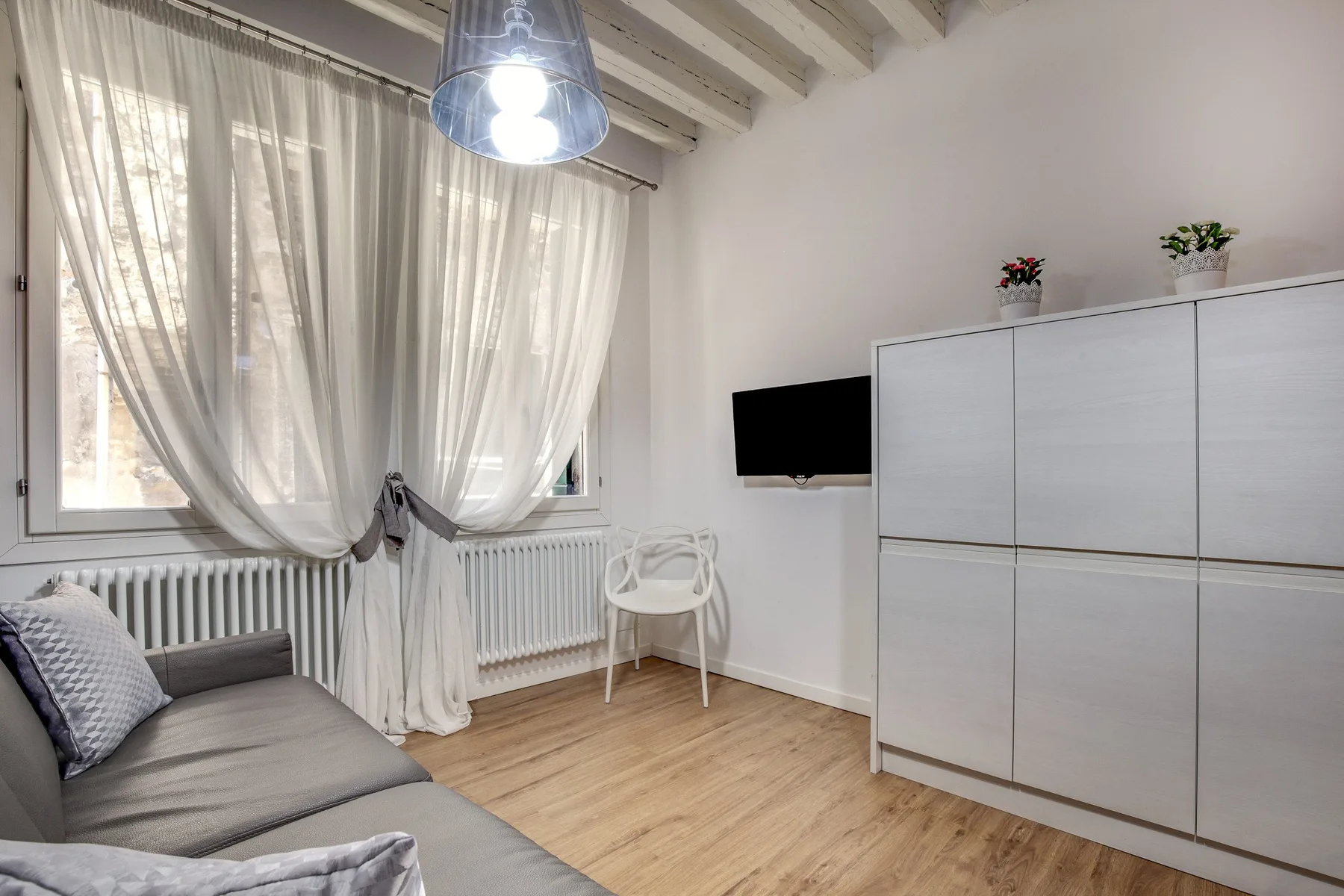 Una sala luminosa con asientos junto a una ventana con cortinas y un televisor en la pared.