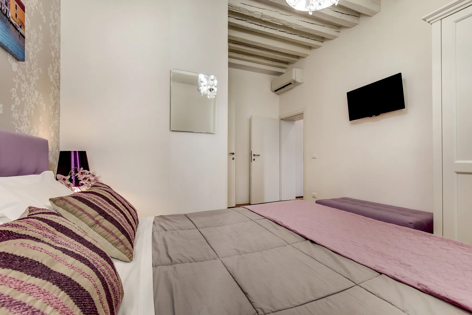 Un dormitorio con camas, un televisor en la pared y vigas expuestas en el techo.