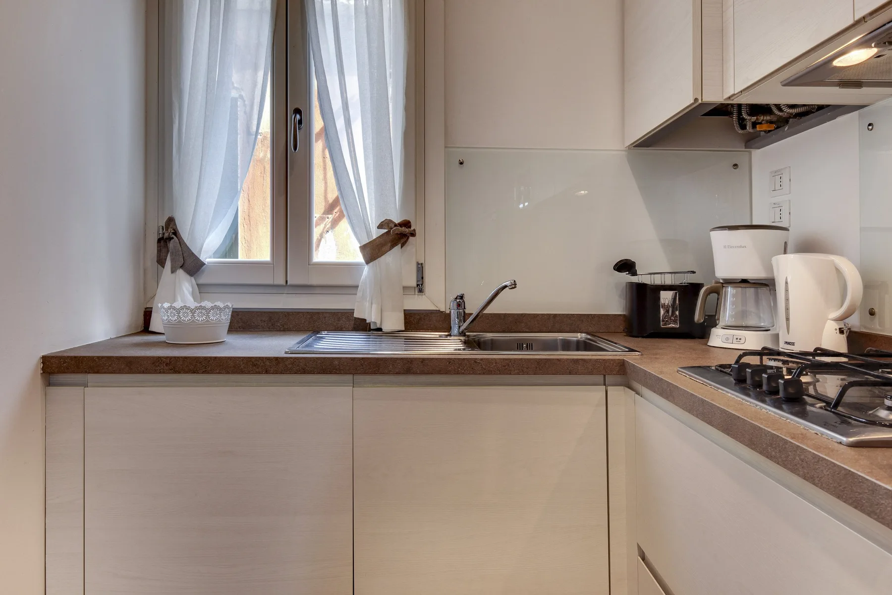 Una cocina luminosa con gabinetes blancos, un fregadero bajo la ventana y una estufa.